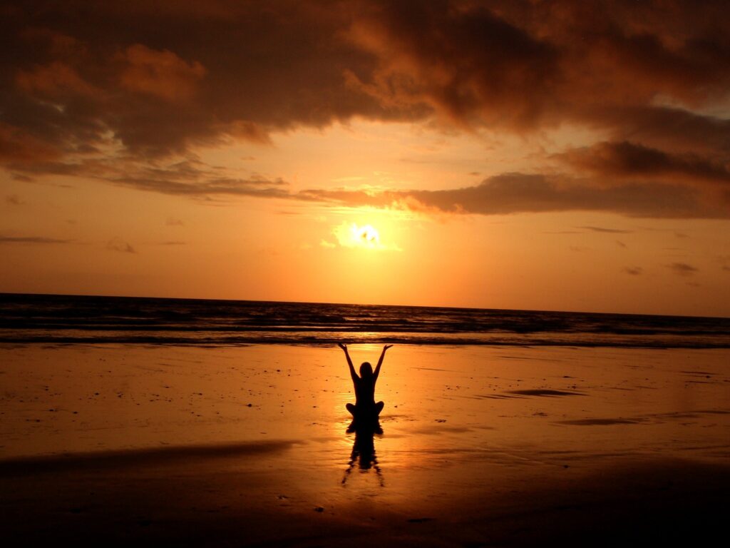 picture of woman meditating on beach arms up